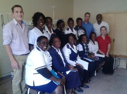 Nurses in uniform and other adults in a group photograph in a hospital room