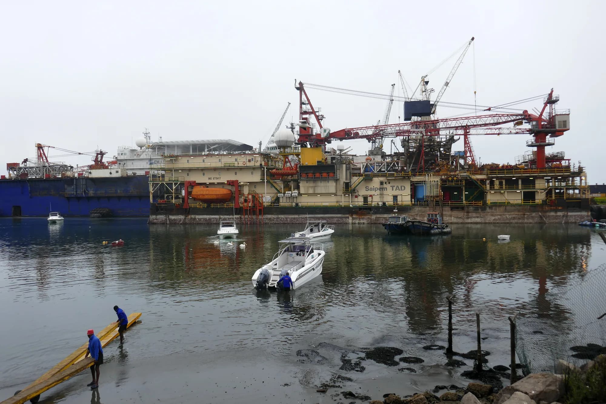 An offshore drilling tender and a supply vessel berthed in the Port of Walvis Bay, with small boats being launched in the foreground